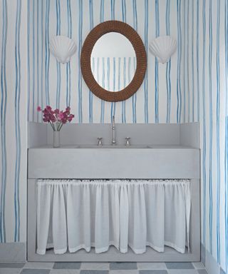 Bathroom with blue and white striped walls with mirror over a vanity with curtained front