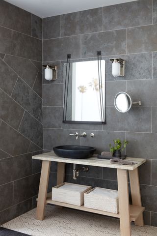 gray bathroom with gray wall tiles floor to ceiling, wooden trestle sink unit, mirrors, wall lights