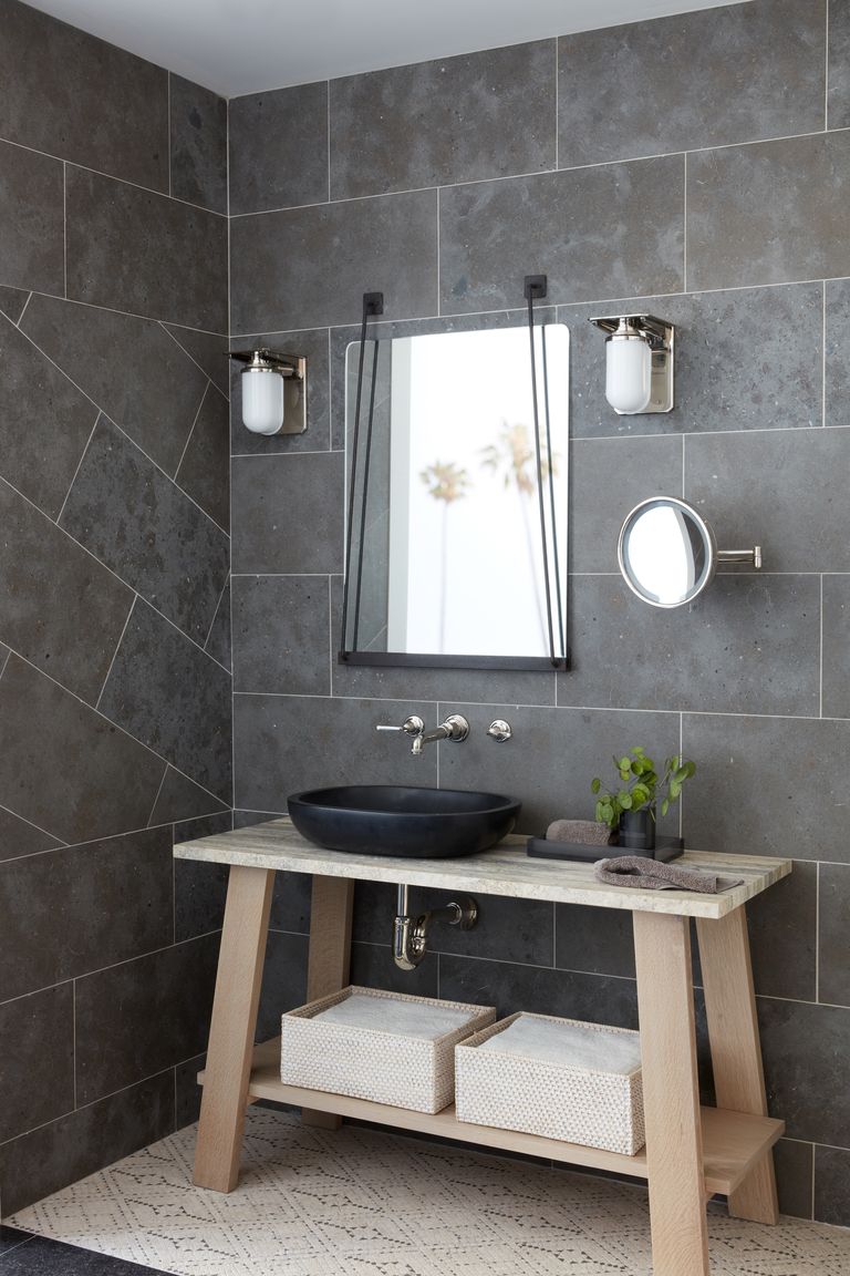 gray bathroom with gray wall tiles floor to ceiling, wooden trestle sink unit, mirrors, wall lights 