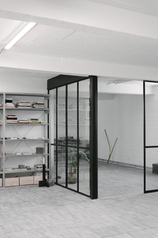 Interior view of the upstairs studio space featuring white painted brick walls, stone tiles, glass partitions and storage space for the designer's archives