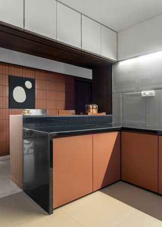 Kitchen with terracotta door fronts, black countertop and steel grey splashback