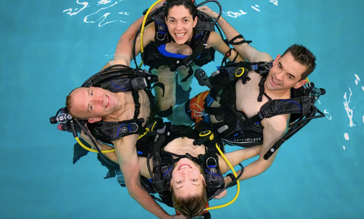 four astronauts in scuba gear holding each other in a pool