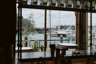 view from bivacco restaurant in auckland out onto harbour through the window, boats on water and tables in foreground