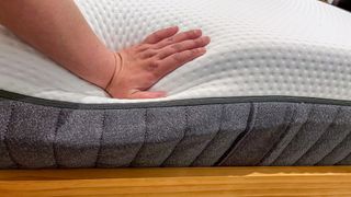 A hand pushing down on the edge of the Emma Luxe mattress