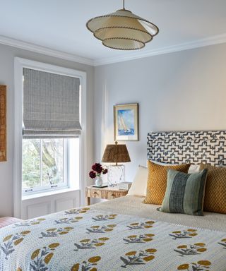colors that go with light grey/light grey bedroom with grey blind, ochre bed pillows, blanket with ochre flowers, artwork, blue patterned headboard