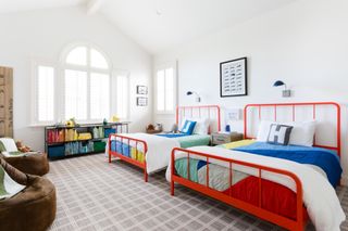 twin beds in kids bedroom painted red, bright bedding, grey check carpet, chairs, bookcase, artwork