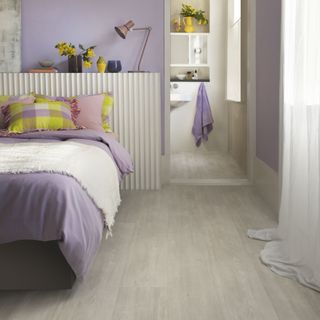 bedroom flooring with light wood flooring, lilac walls and throw, ensuite, shelf behind bed, yellow accents