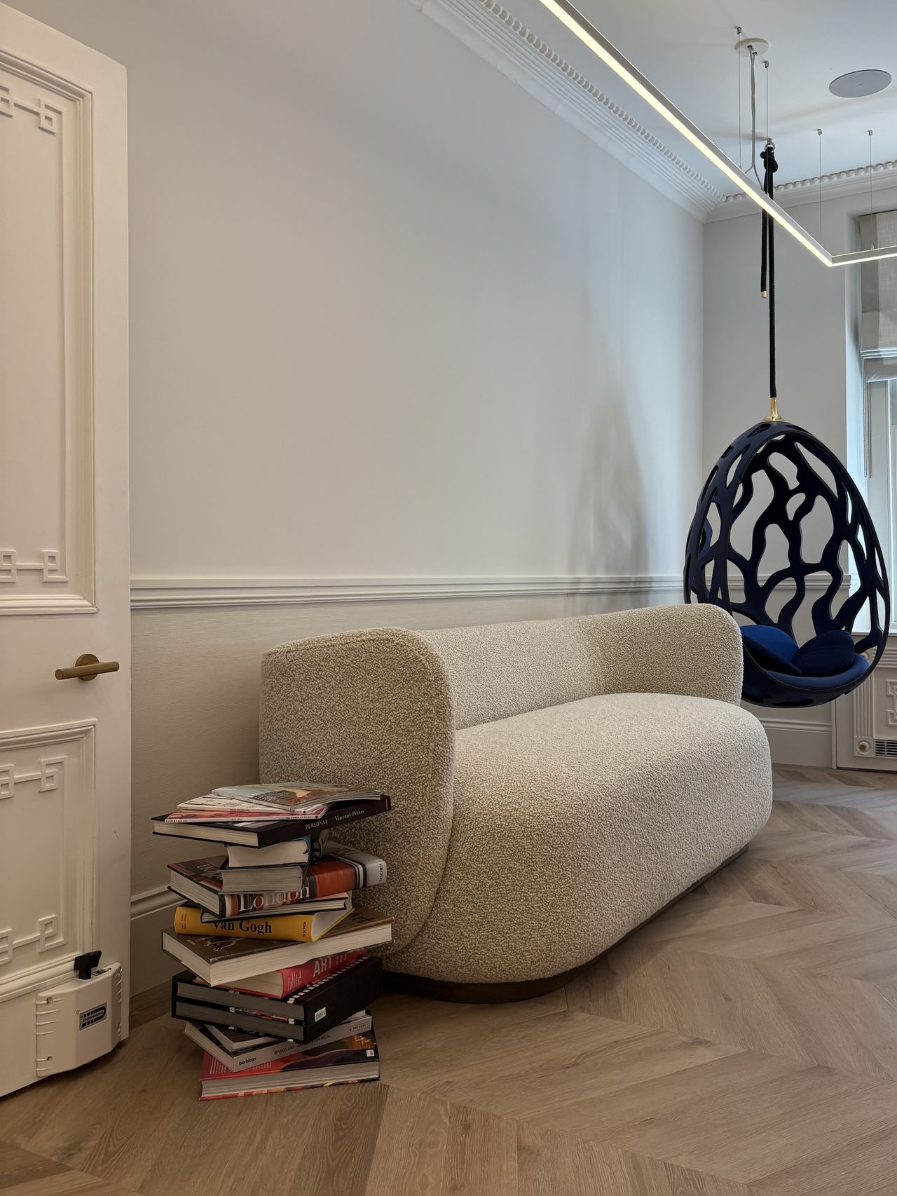 A sumptuosly furnished historical townhouse features a stack of glossy coffee table books, an oversized boucle couch, and a hanging egg-shaped blue chair among its standout features.