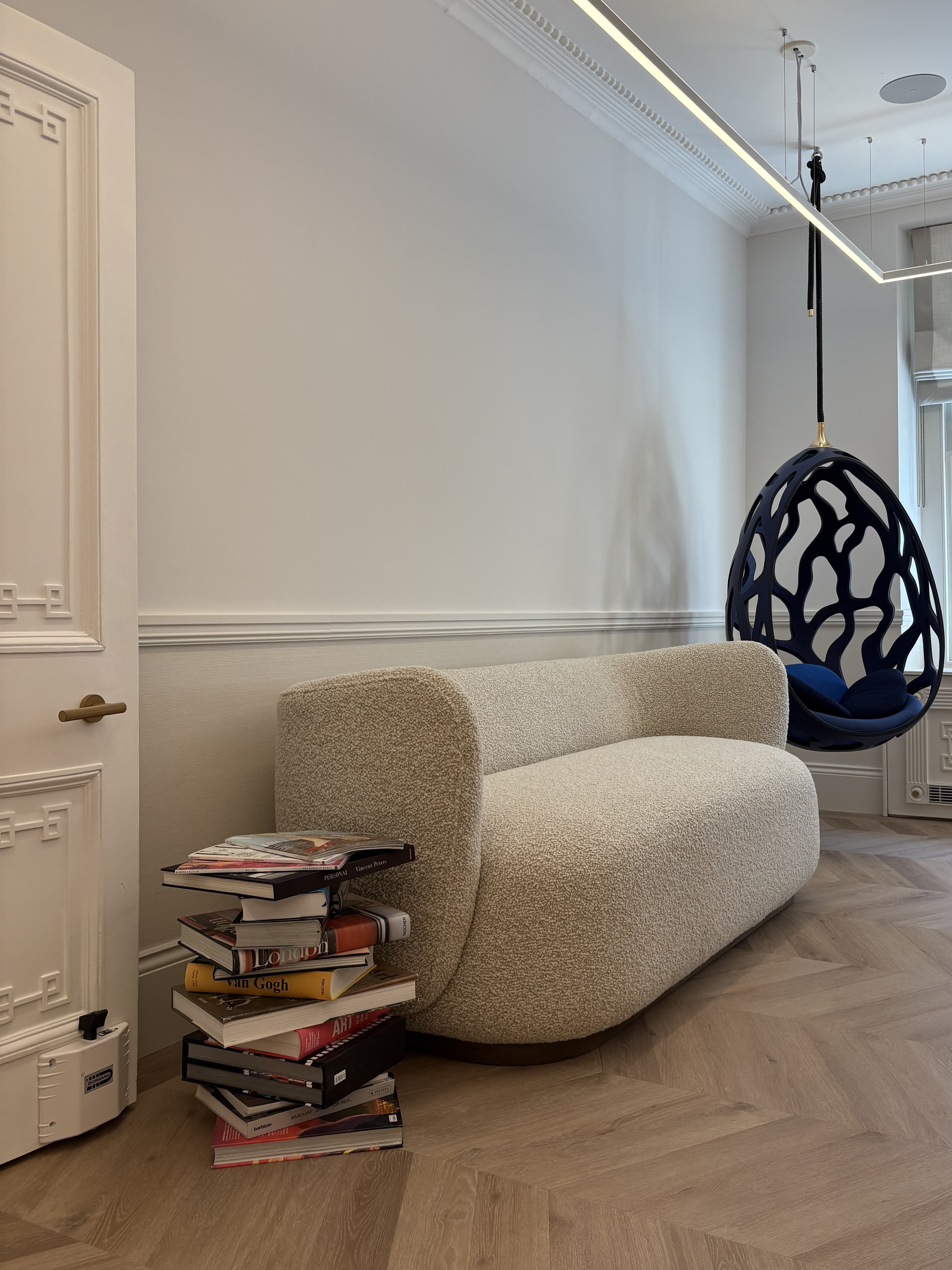A sumptuosly furnished historical townhouse features a stack of glossy coffee table books, an oversized boucle couch, and a hanging egg-shaped blue chair among its standout features.