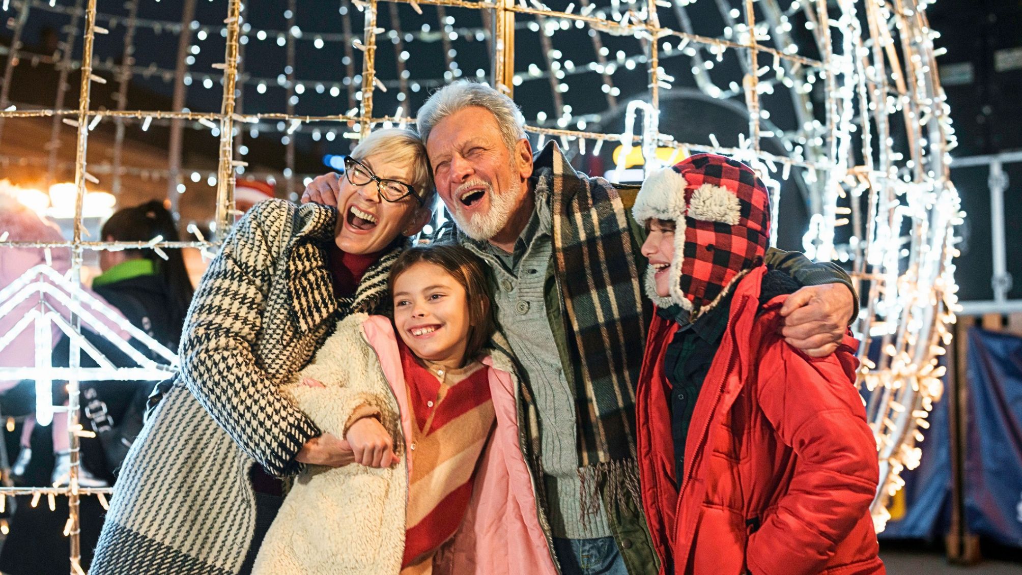 Smiling grandparents embracing their young grandson and granddaughter at a holiday event