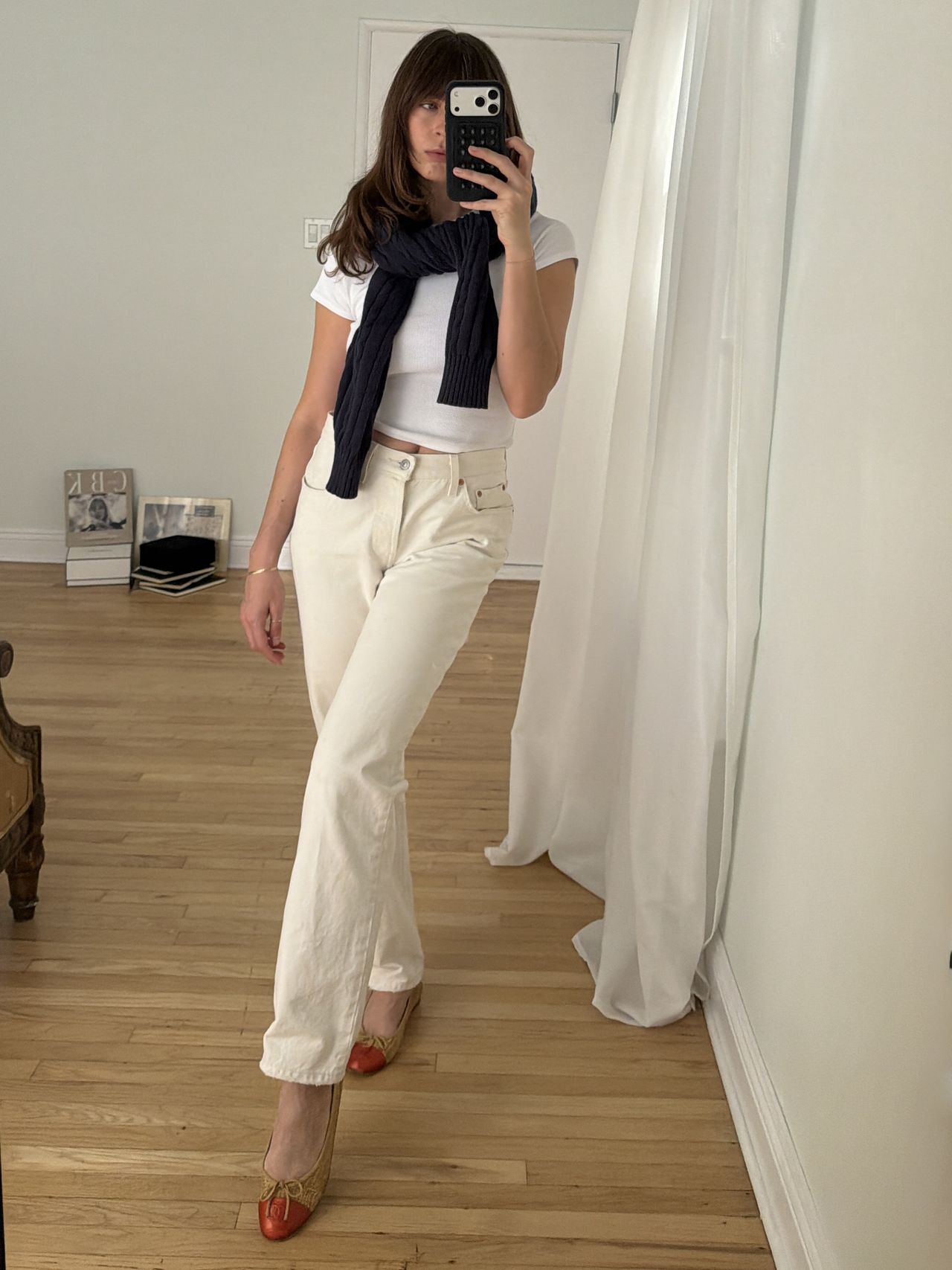 Kathryn Zahorak posing in mirror wearing white jeans, white t-shirt, navy sweater, and red cap ballet flats