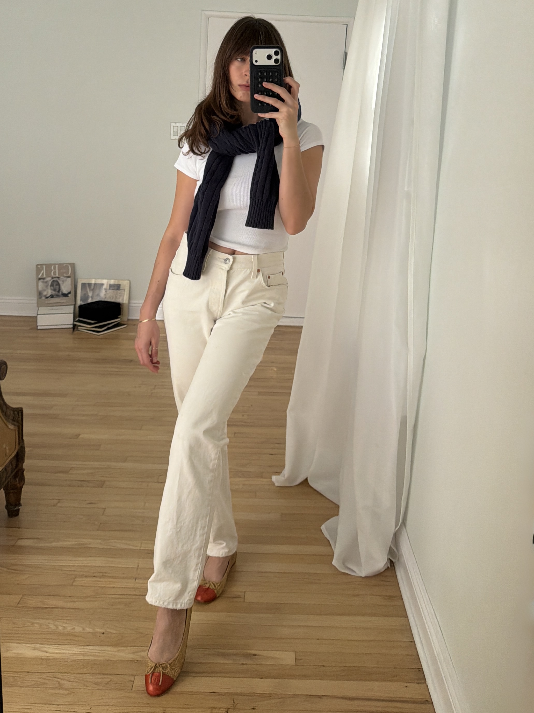 Kathryn Zahorak posing in mirror wearing white jeans, white t-shirt, navy sweater, and red cap ballet flats