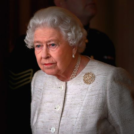 Queen Elizabeth wearing a white tweed jacket and brooch looking out a window