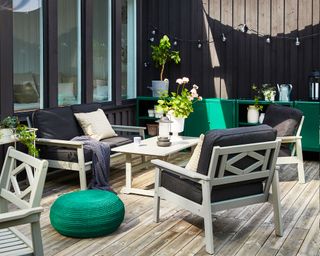 An example of how to make a small garden look bigger with black walls, decking, a canopy and green and black accessories.