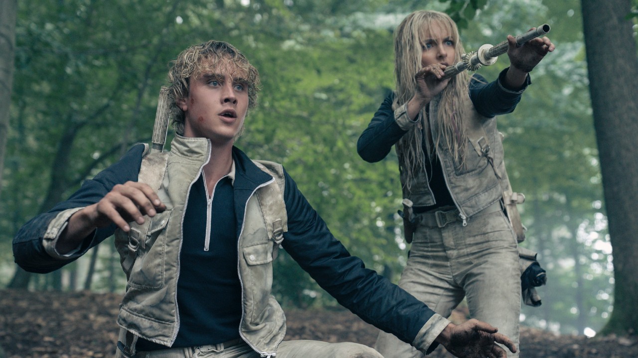 From left to right: Joseph Zada kneeling with his arms out and he looks shocked. McKenna Grace standing behind him and holding up a blowdart in Sunrise on the Reaping.
