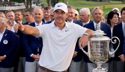 Koepka points whilst posing next to the trophy