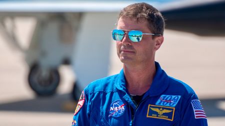 An astronaut in blue jumpsuit stands outside.