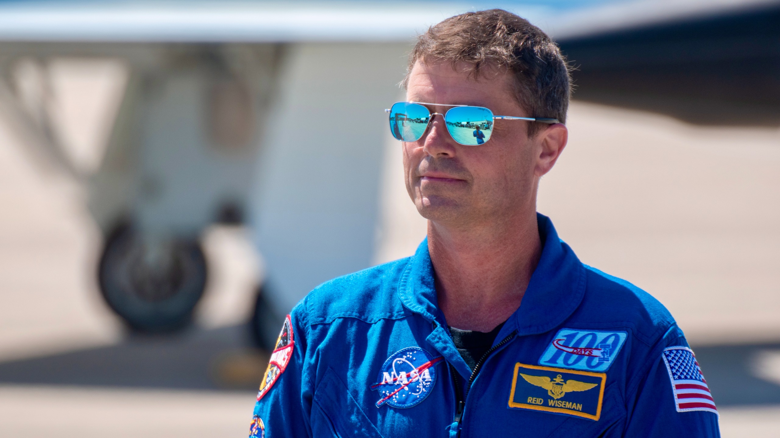 An astronaut in blue jumpsuit stands outside.