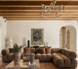 A living room with wooden beams, a large brown rug, and a large curved cloud sofa in a brown color