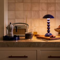 Addison Ross bobbin lamp in navy on a kitchen worktop with a round scalloped matching tray, a Roberts radio and an Alessi espresso maker