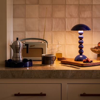 Addison Ross bobbin lamp in navy on a kitchen worktop with a round scalloped matching tray, a Roberts radio and an Alessi espresso maker