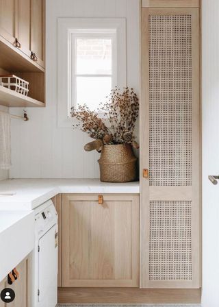 Neutral small laundry room ideas with natural wood textured cabinets and dried flowers by a white countertop and backsplash.