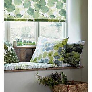 window seat with leave patterned cushions, blinds and a basket on the floor with plants inside