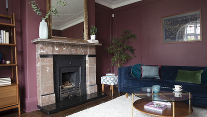 Burgundy living room with blue velvet sofa, pink marble fireplace with ornate gold mirror, gold and walnut coffee table and cream oversized rug