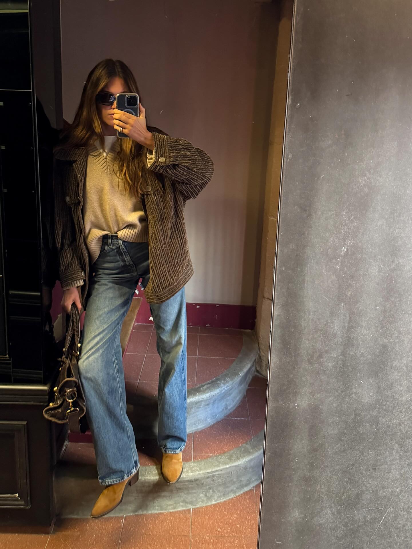 An image of @saraloura wearing fitted bootcut jeans with a beige V-neck sweater.