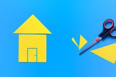 A house cut out of yellow paper on a blue background with scissors nearby