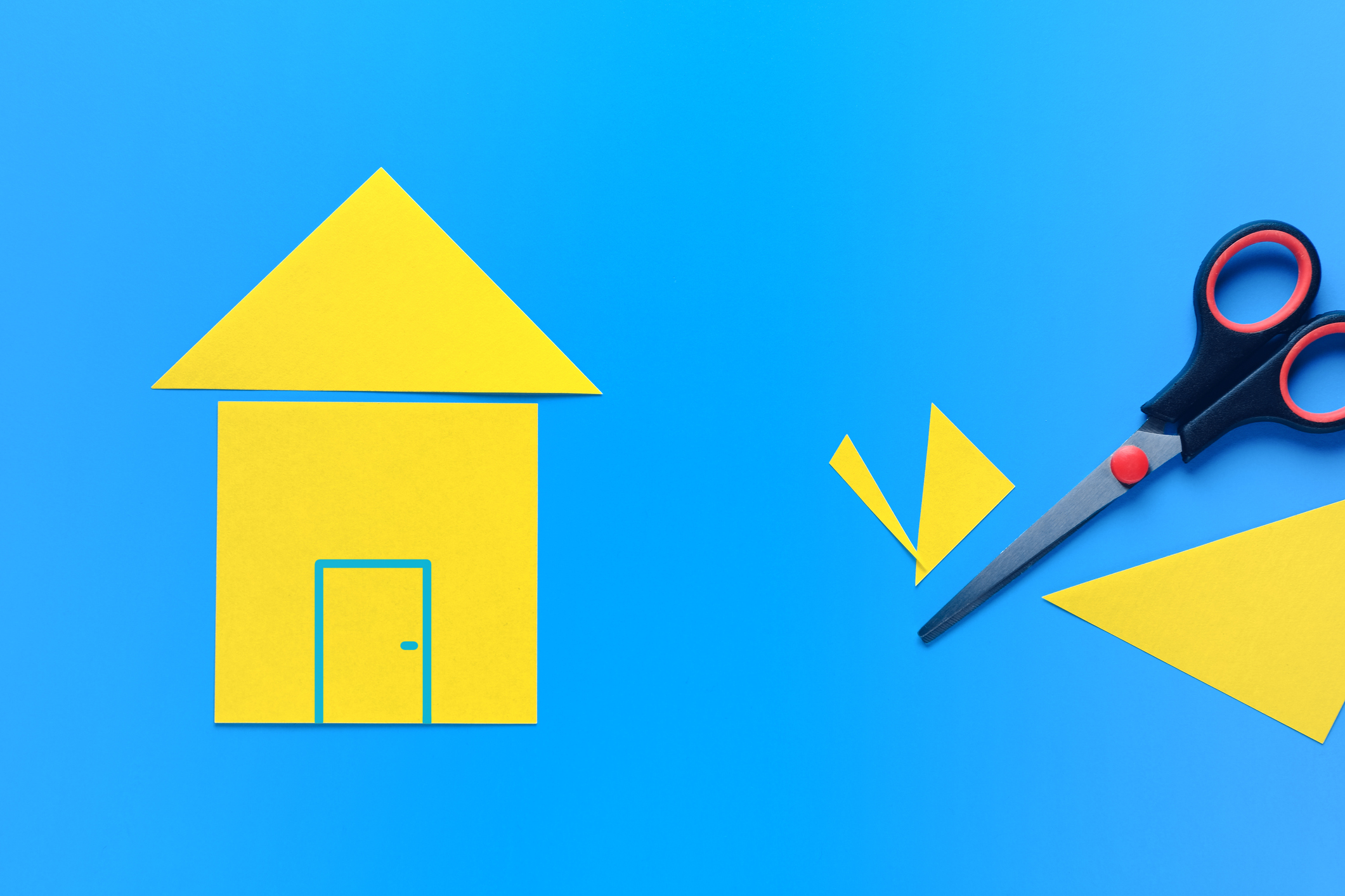 A house cut out of yellow paper on a blue background with scissors nearby