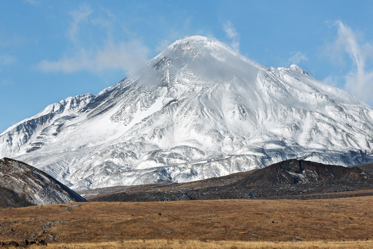 Bezymianny volcano covered in snow and ice with grass in foreground