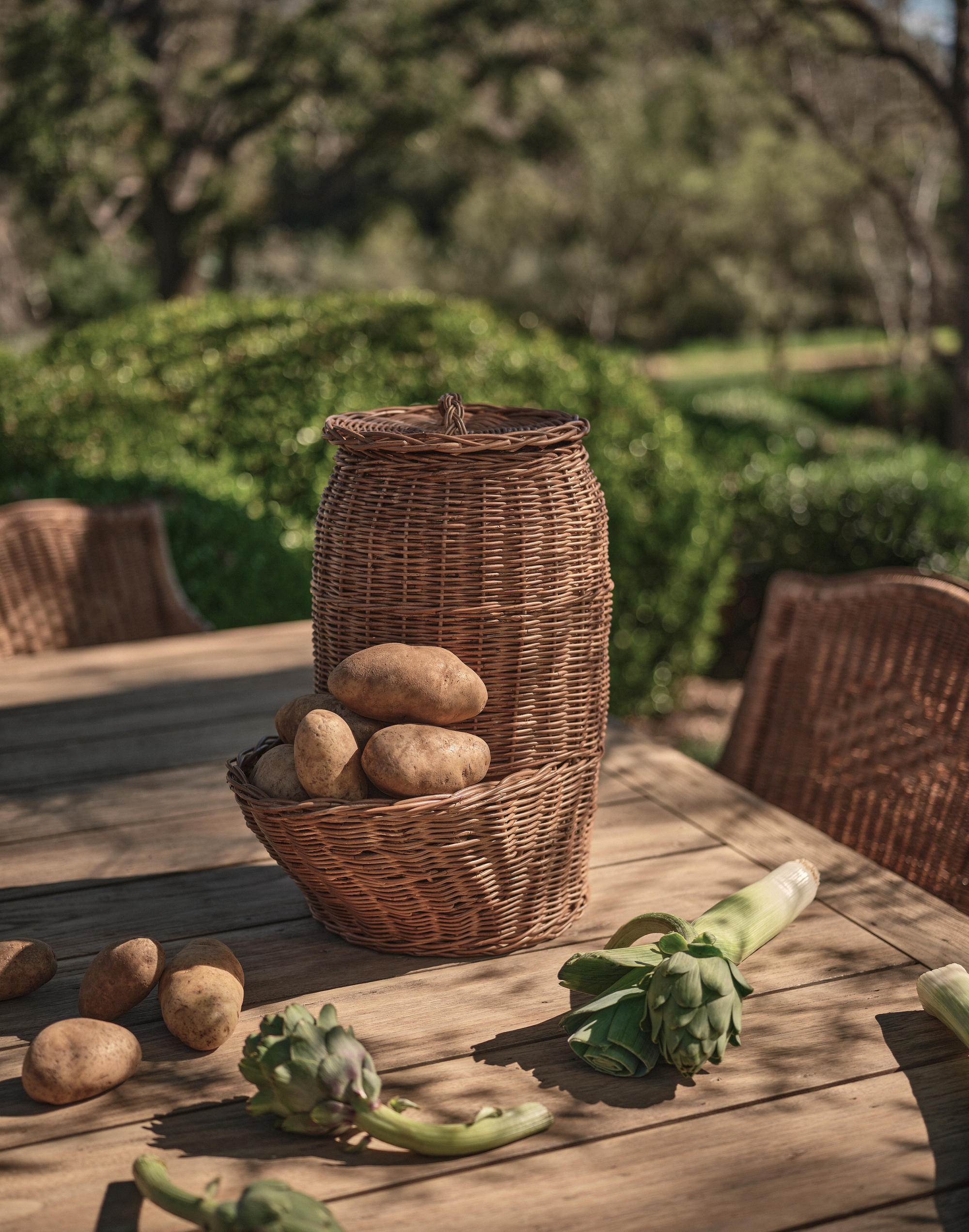 close up of outdoor table with rattan potato holder with potatoes and artichokes