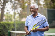 An older man grins as he holds a tennis racket on the court.