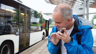 A blind man using a phone next to a bus, to represent an example of generative AI being used for accessibility.