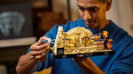 A man in a blue jumper holds up the Lego Mos Espa Podrace Diorama