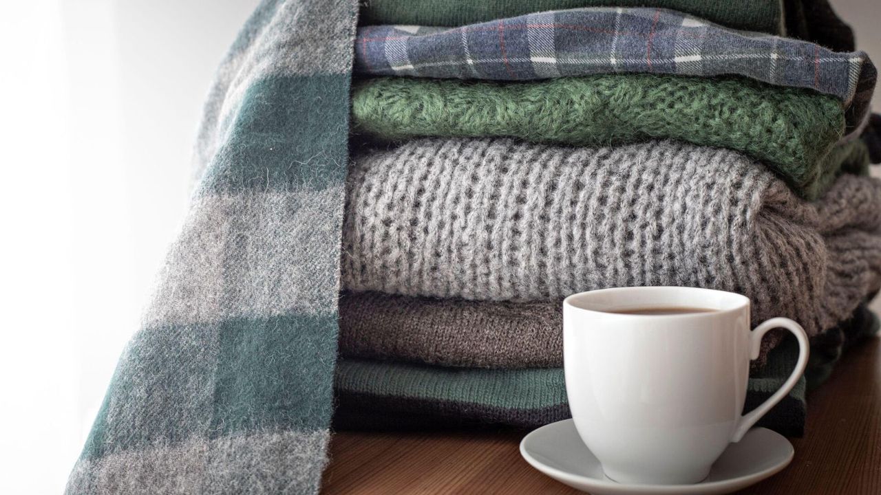 A pile of folded jumpers beside a teacup