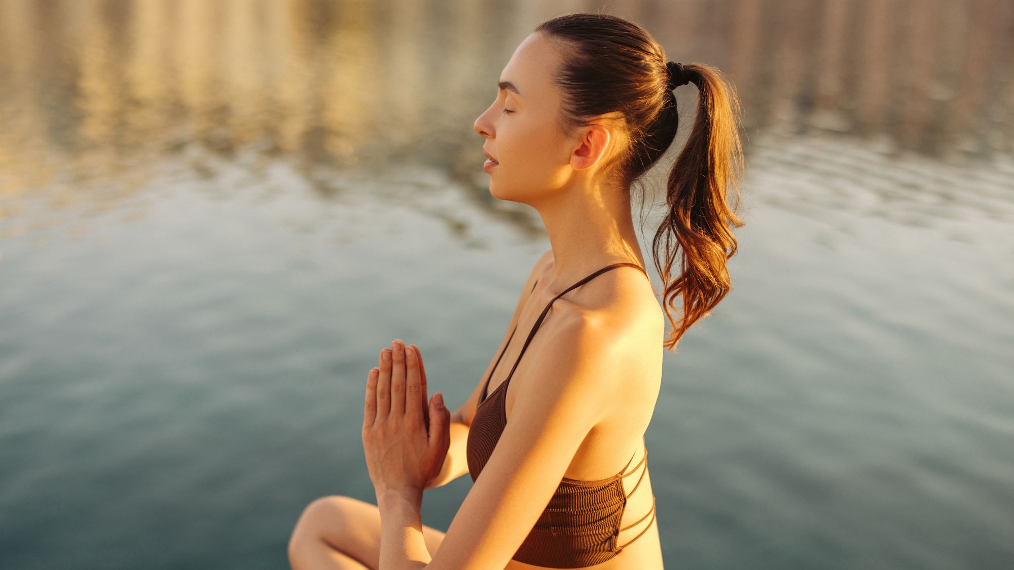 A woman meditating by a lake as part of her September reset