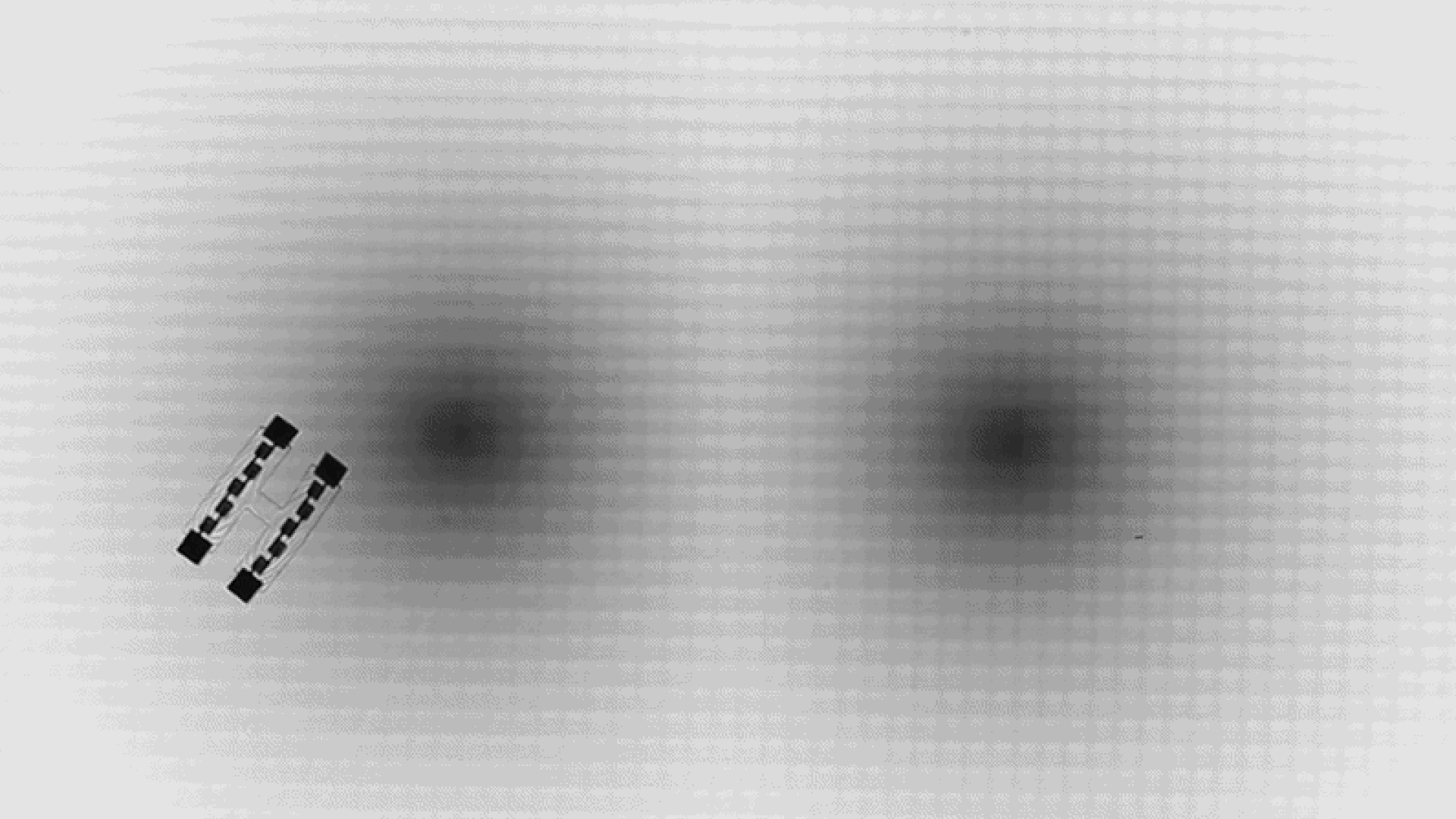 A gif showing two dark lines parallel to each other moving circularly from bottom left to top right around two dark blurry circles in the center of the image