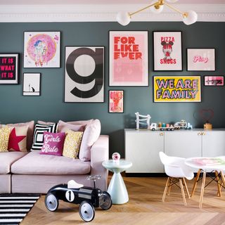 family toom with dark blue walls and a gallery wall of prints a pink sofa and a kids' table and chairs