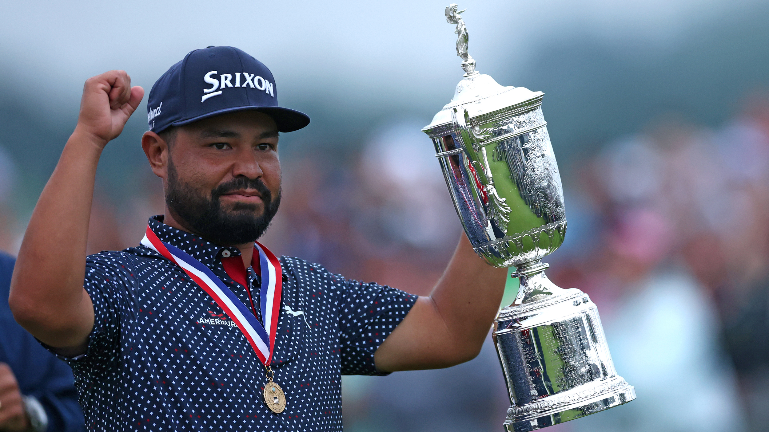 JJ Spaun raises his right fist up to the sky while holding the US Open trophy in his left