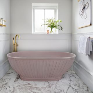 Pink fluted freestanding bath in front of a window in a white bathroom