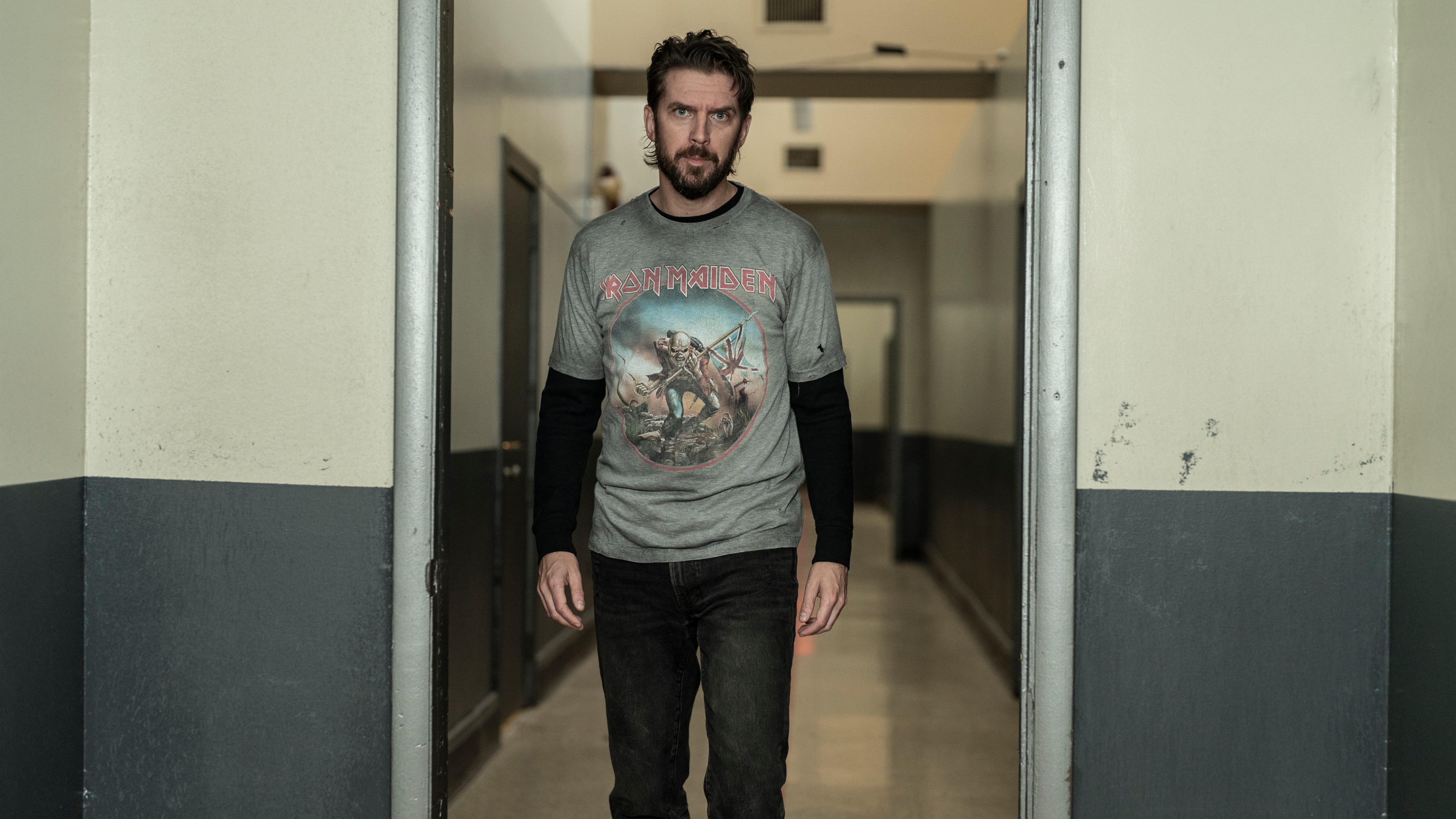 Dan Stevens as Pepper wearing a grey Iron Maiden t-shirt walking down a prison corridor.