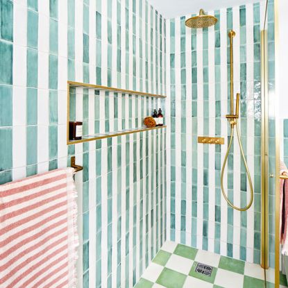 walk-in shower with striped green and white wall tiles, shower niche and brass showerhead