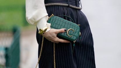 Woman wearing oud nails, one of the best winter nail colours for 2023, at Paris Fashion Week while holding a green Celine clutch bag
