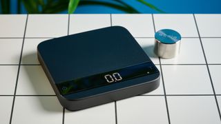 the acaia lunar coffee scale in black with an aluminum surface and accurate precise weight ideal for espresso machines given its compact size is photographed againt a blue tom's guide background