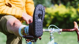 A rider props their heel up on a brown brooks saddle, revealing a cleat on the underside of a brown boot