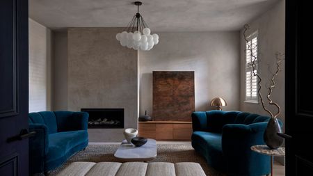 A living room with double doors that have been opened leading to two blue colored sofas and a coffee table in the middle of the sofa 