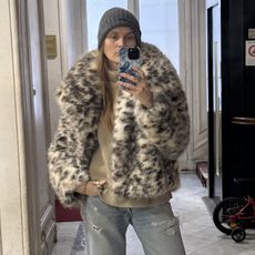 French writer and editor Eugenie Trochu poses for a mirror selfie wearing an animal-print faux-fur print coat, a gray beanie, tan sweater, distressed ripped jeans, and Timberland boots