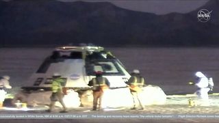 a cone-shaped spacecraft on the desert floor surrounded by people in hard hates